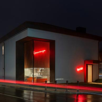 Edificio bianco con ampie vetrate, insegna rossa al neon accesa su due pareti, fotografato di notte.