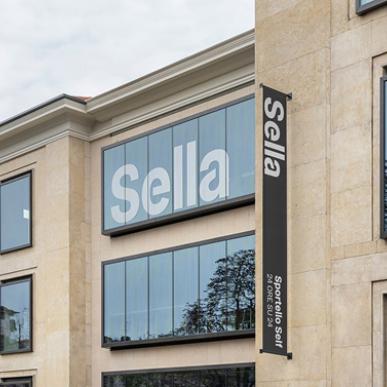 Open space luminoso con scrivanie in legno chiaro, sedie ergonomiche e persone al lavoro.