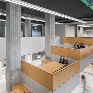 Interno con postazioni di lavoro a gradoni in legno, usate da persone al computer.