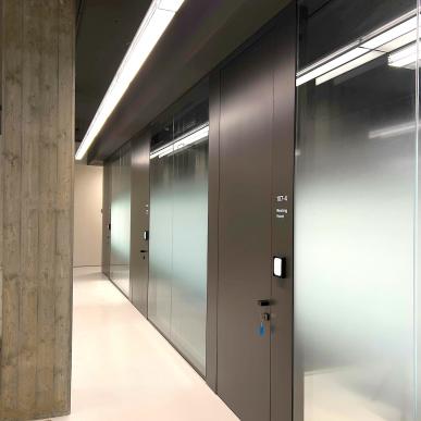 Corridoio con porte scure e vetrate satinato che conducono a sale riunioni.