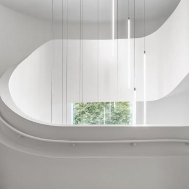 Scala interna elicoidale bianca con ringhiera curva e lampade sospese verticali.