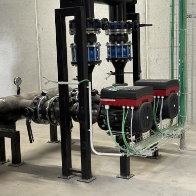 Pompe industriali elettriche collegate a un sistema di tubazioni nere con valvole e raccordi.