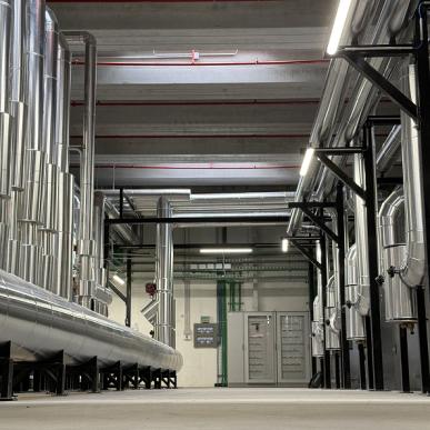 Corridoio tecnico interno con grandi tubazioni in acciaio inox e impianti industriali ai lati.