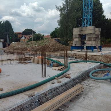 Foto del cantiere con fondamenta in costruzione, tubazioni e armature in acciaio per la nuova scuola.