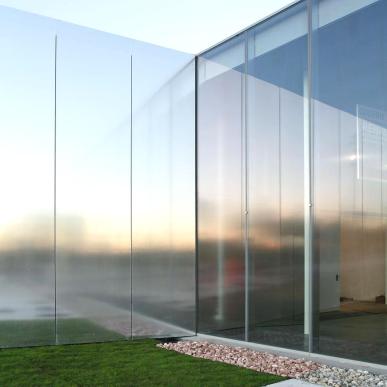 Dettaglio di un edificio della scuola con facciata in vetro satinato e area esterna con prato e ghiaia decorativa.