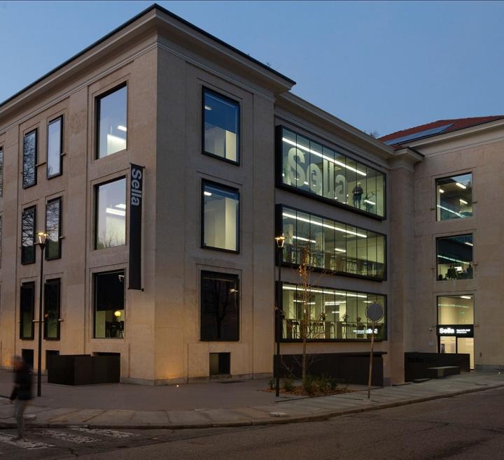 Sede Sella in un edificio a più piani con facciata in pietra e grandi finestre luminose su strada.